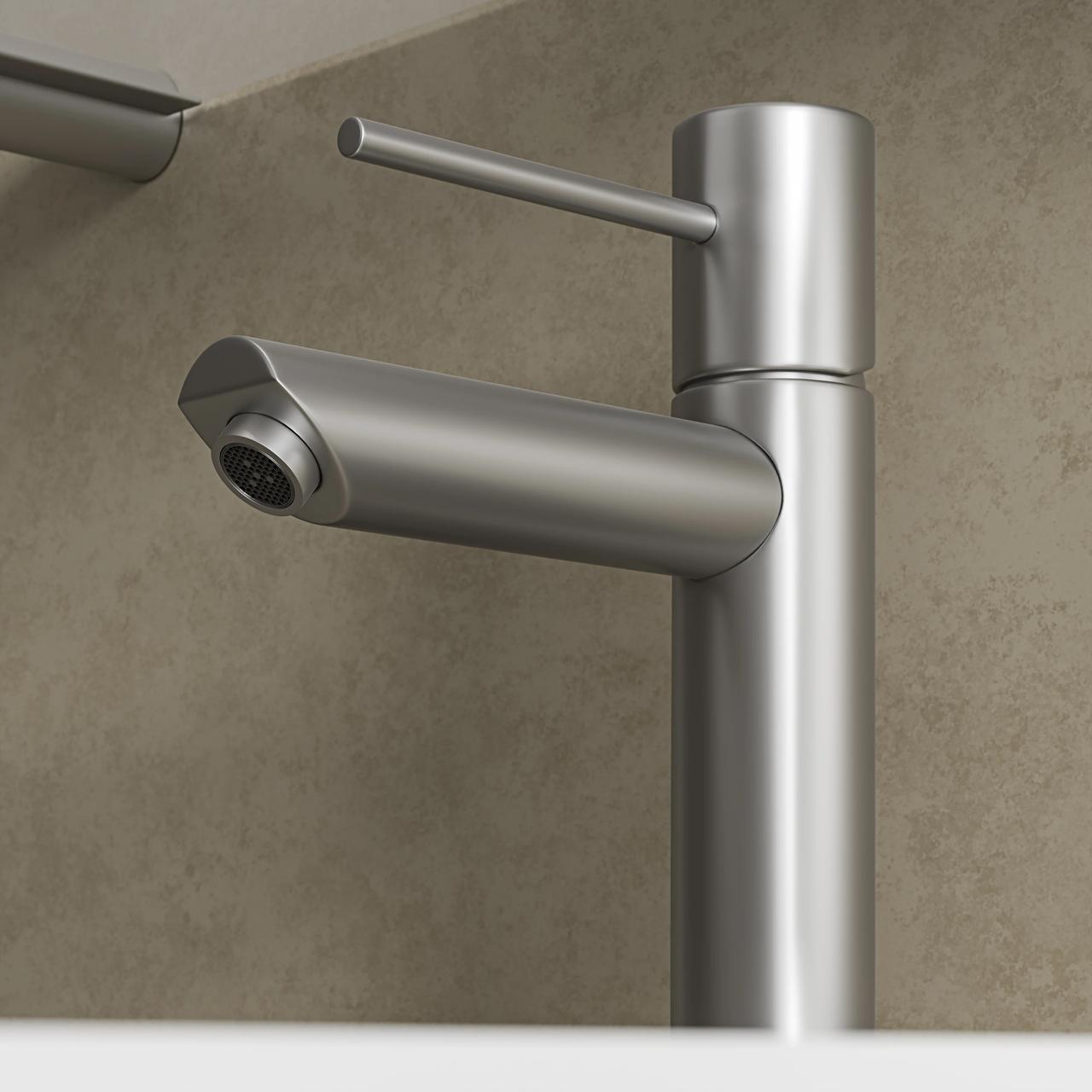 A highly detailed close-up of a modern cylindrical 3d bathroom faucet finished in brushed stainless steel. The shot sharply focuses on the slim lever handle and the mesh aerator in the spout, set against a softly blurred warm grey stone background.