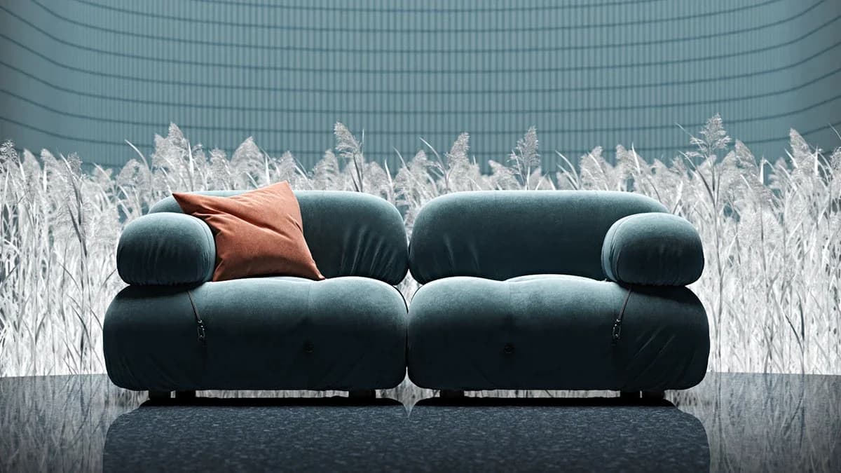 Plush modular teal-blue sofa with a terracotta accent pillow set against a grid-patterned light blue wall and white dried reeds