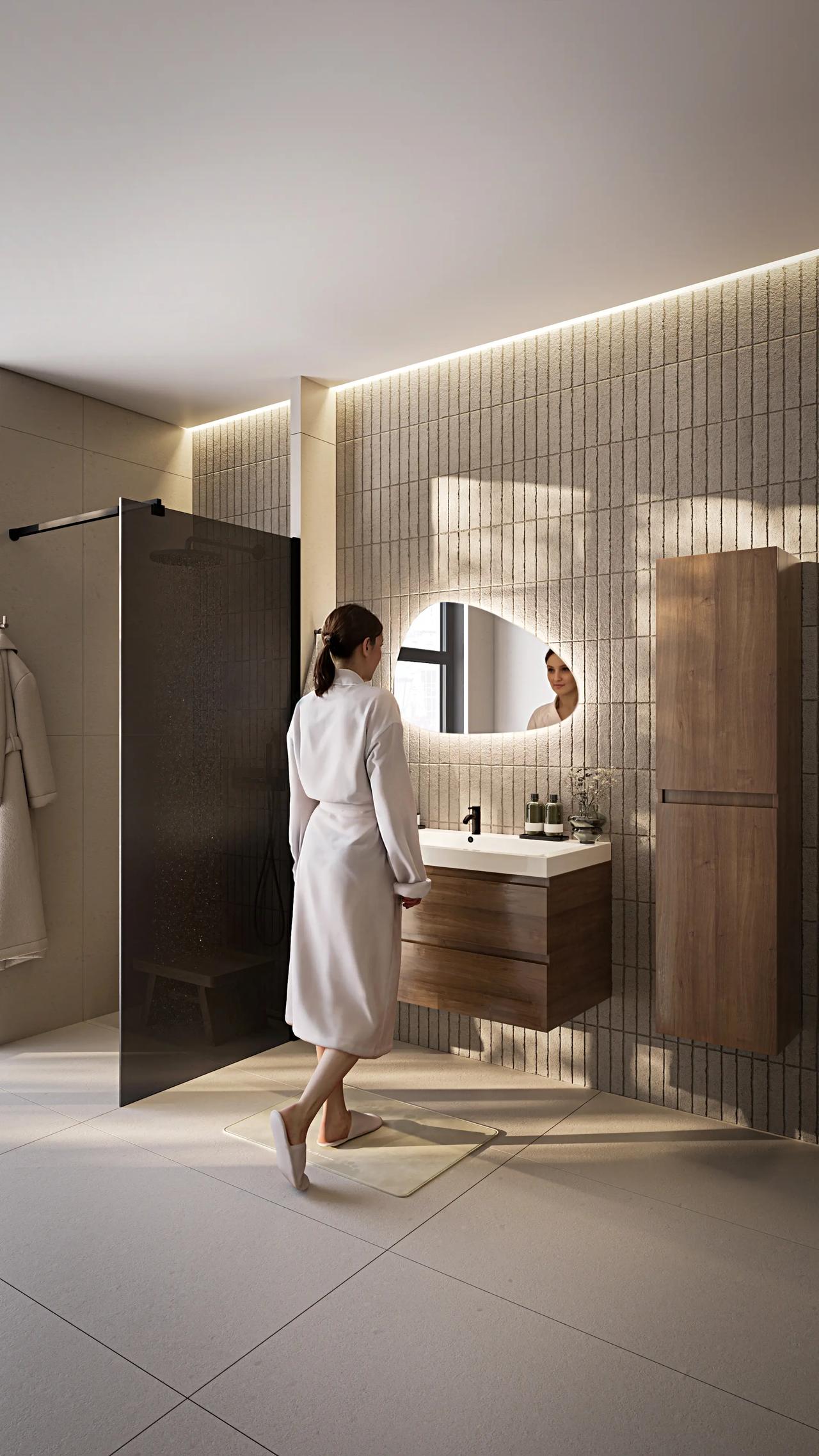 Vertical full-length shot of a woman in a bathrobe walking through a spacious modern bathroom with led-lit vertical tile walls, a vanity unit, and a glass shower cabin