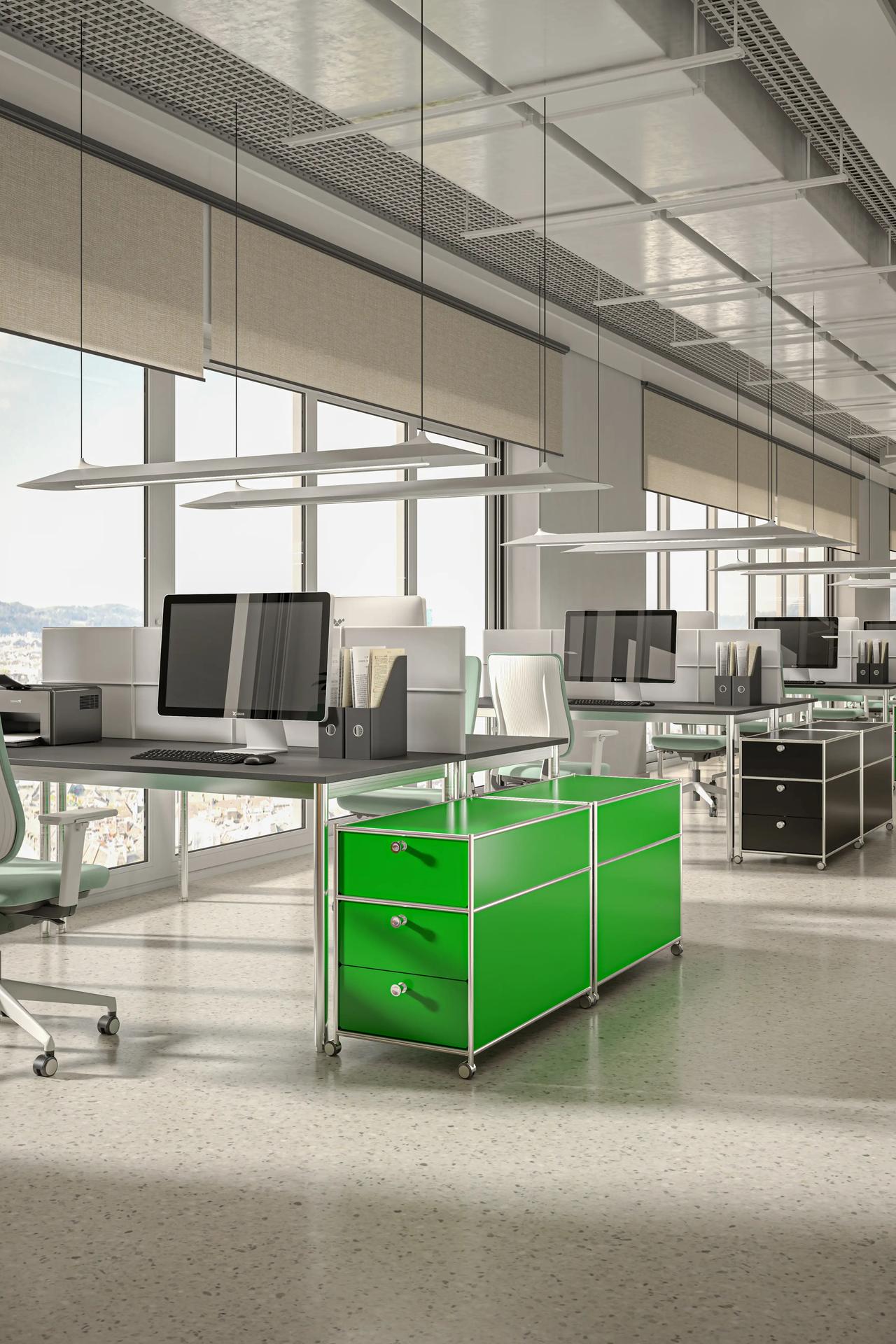 A modern open-plan 3d office featuring a vibrant green metal modular cabinet next to grey workstations with computer monitors. The industrial setting includes an exposed ceiling with linear pendant lights, large windows with roller blinds, and a polished light floor.