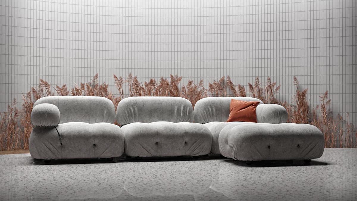 Plush modular light grey sofa with a terracotta accent pillow set against a grid-tiled wall and decorative dried reeds