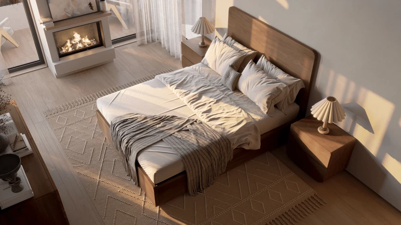 Warm, sunlit modern bedroom featuring a solid wood bed with neatly layered beige linens, matching nightstands with pleated lamps, a geometric area rug, and a burning fireplace in the background