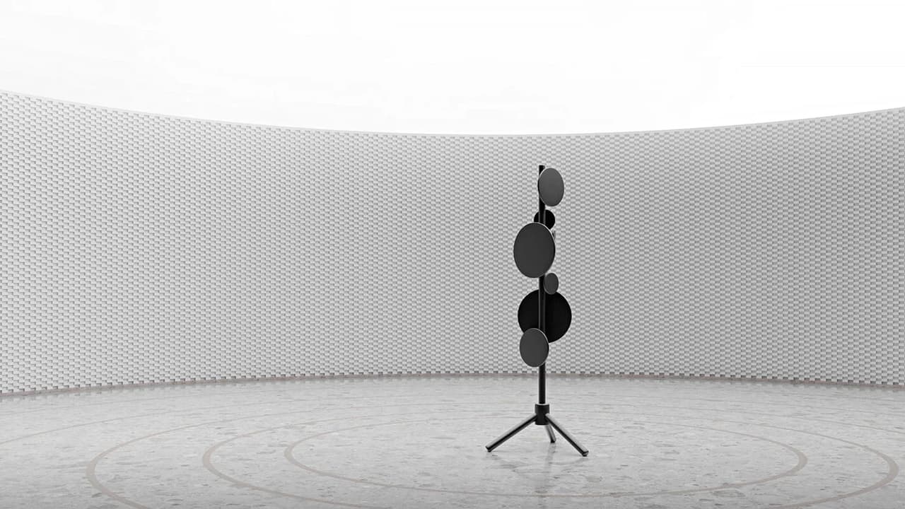Black avant-garde floor sculpture with circular discs on a tripod stand in a spacious minimalist hall with a curved patterned wall