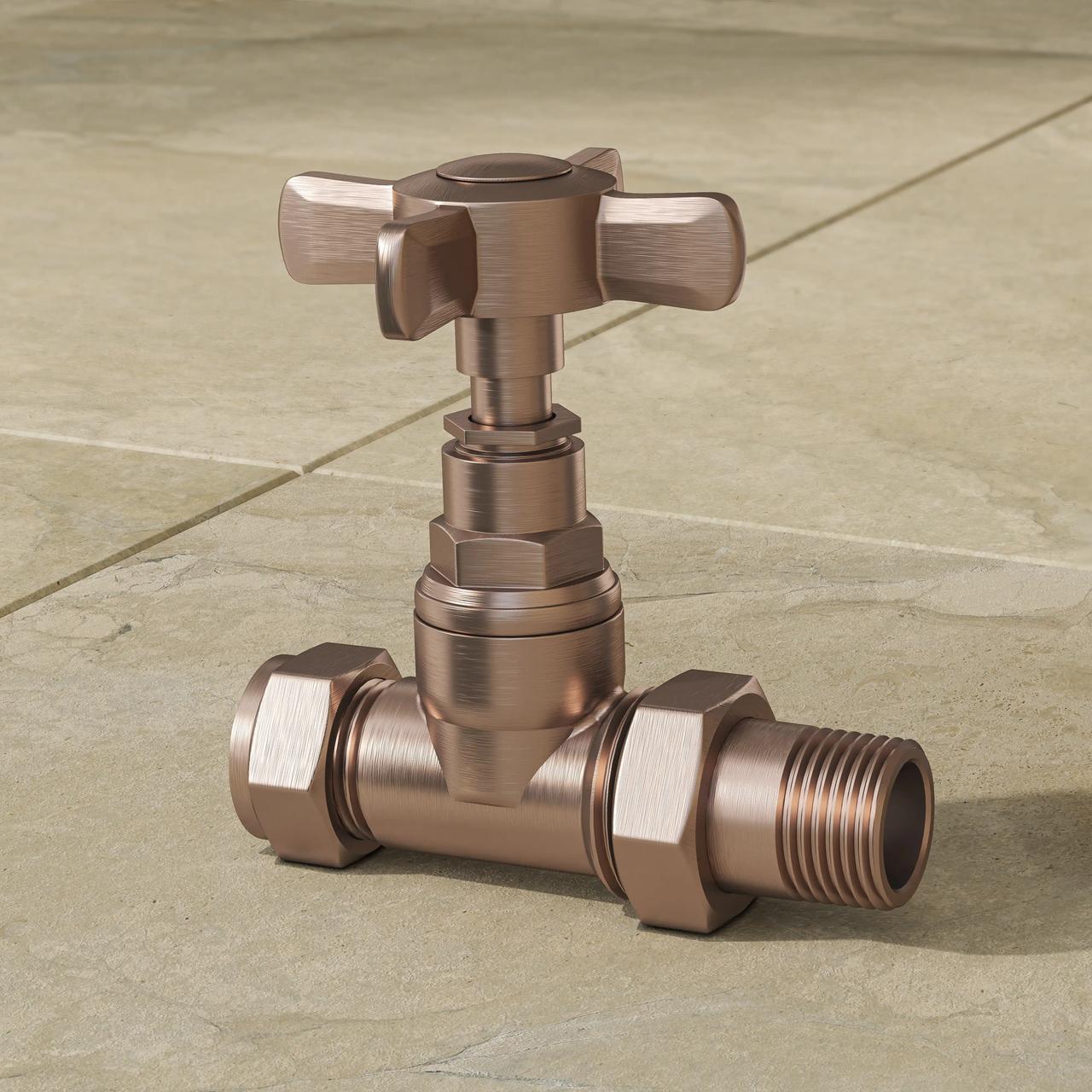A detailed close-up of a vintage-style 3d radiator valve with a cross-head handle, finished in brushed bronze. The metallic plumbing fixture rests on light beige square floor tiles, highlighting its realistic brushed texture and soft shadows.