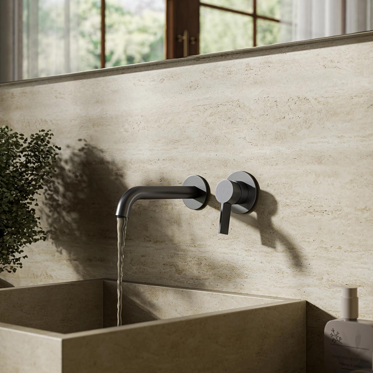 Wall-mounted dark gunmetal tap with running water flowing into a stone vessel sink, set against light textured bathroom wall tiles