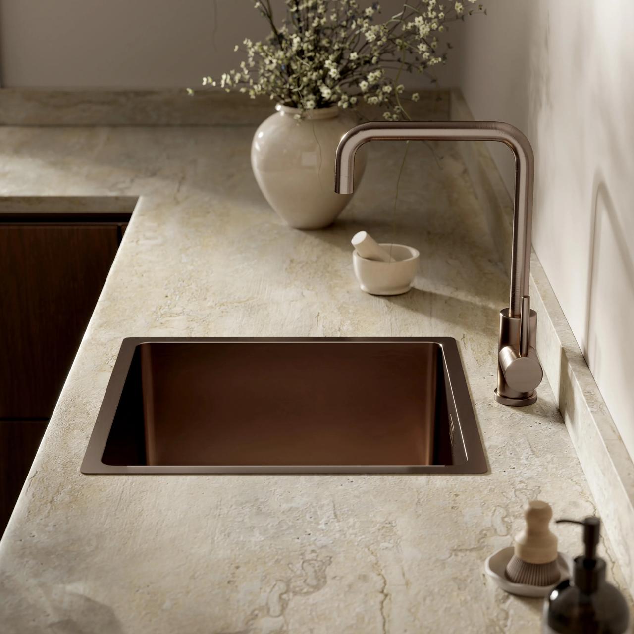 Brushed copper square kitchen sink and matching high-spout faucet integrated into a light marble countertop with modern kitchen accessories