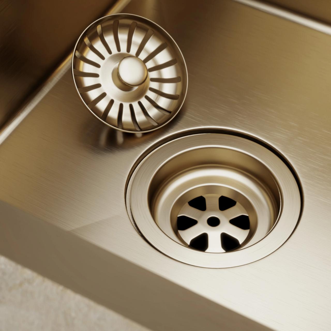 Detailed macro shot of a brushed gold kitchen sink drain with a removable metallic strainer basket on a stainless steel surface
