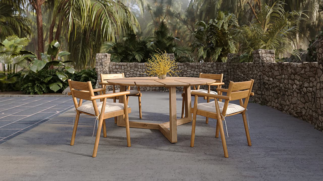 A photorealistic 3D render of a round teak outdoor dining table surrounded by four matching wooden armchairs with cream cushions. The set is placed on a dark stone patio framed by a natural stone wall and lush tropical palms under warm natural light.