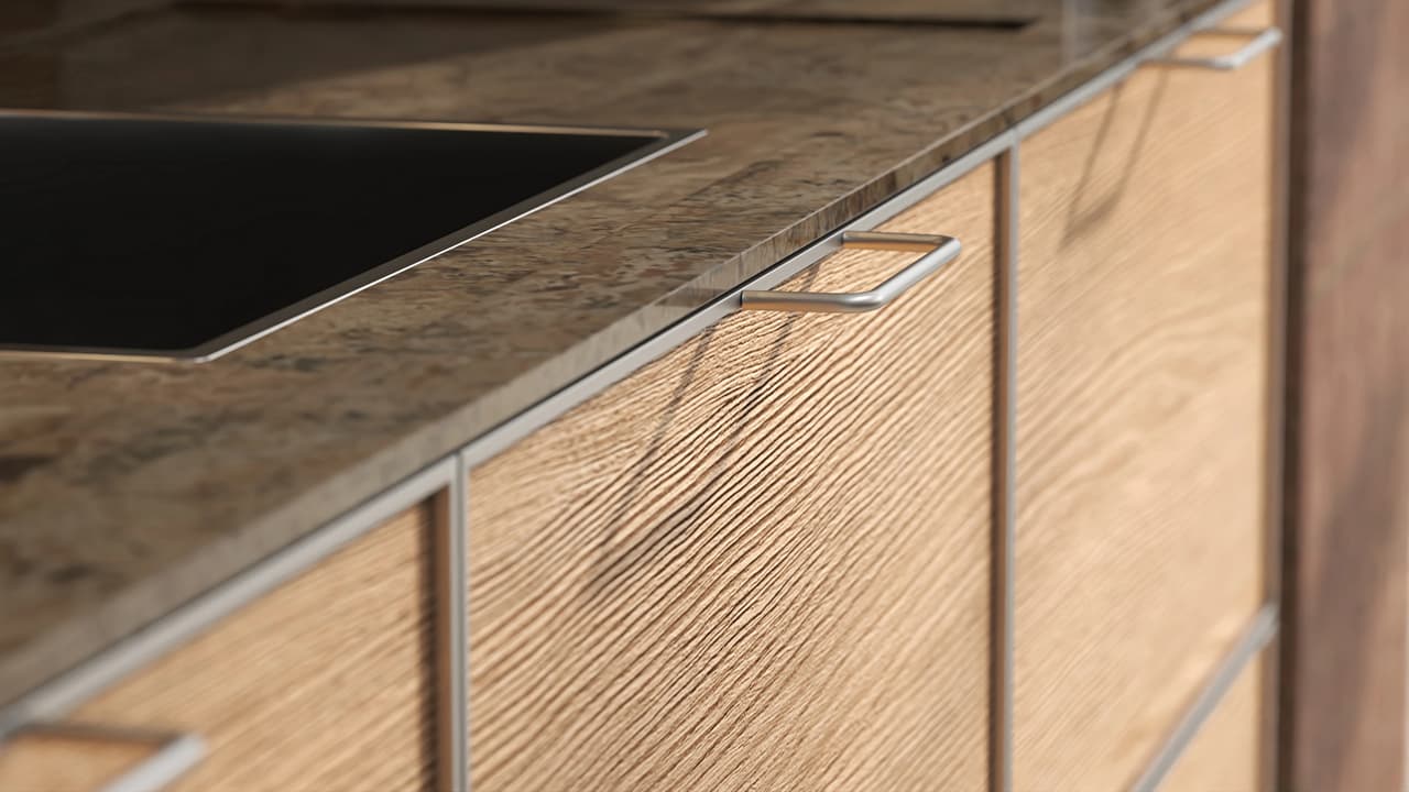 A close-up shot of modern cgi kitchen cabinetry featuring ribbed light wood fronts and minimalist brushed metal handles. The sharp focus highlights the deep wood grain texture, contrasting softly with a polished brown stone countertop and a blurred black cooktop in the background.