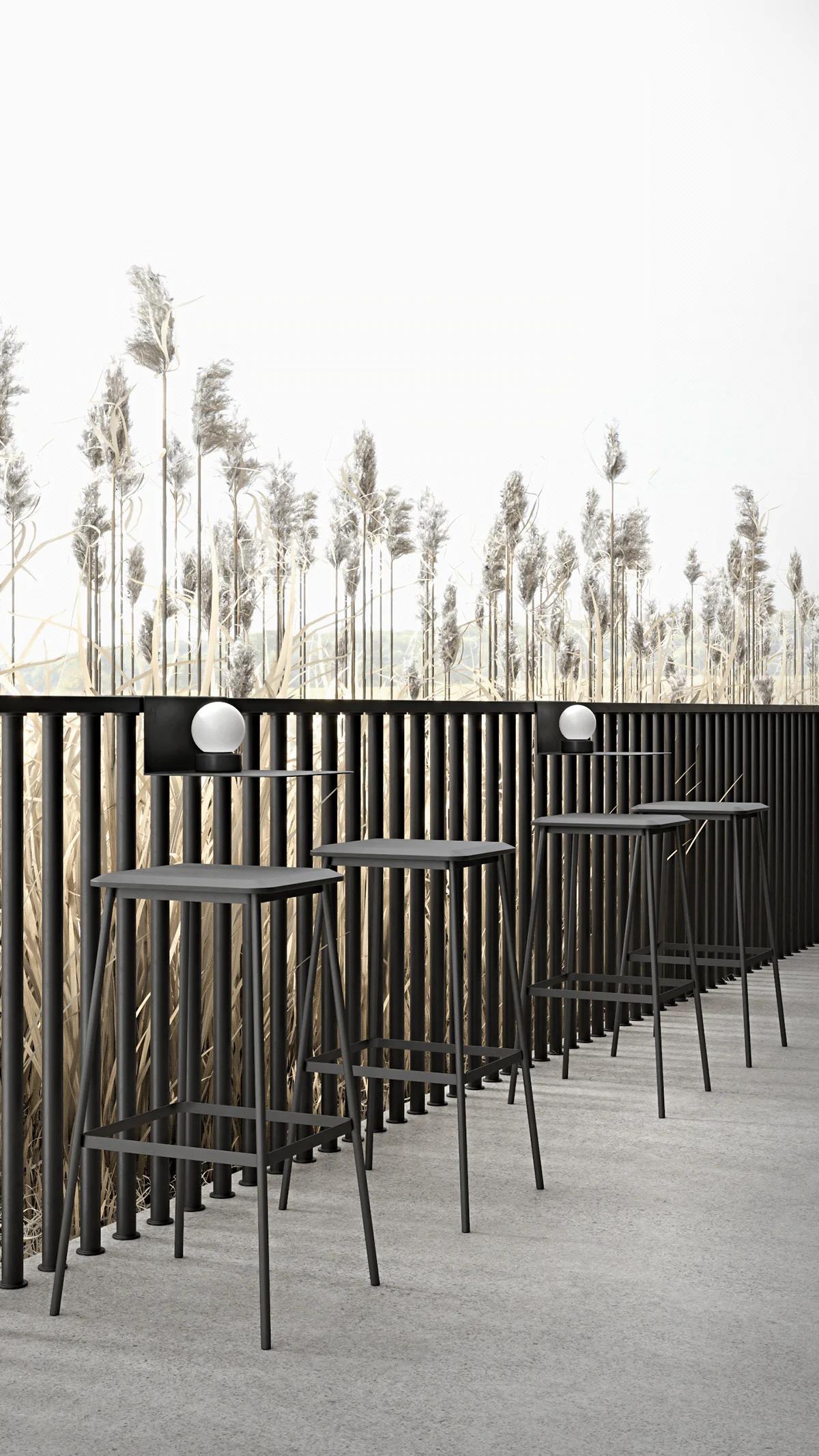 Vertical view of a tranquil outdoor cafe terrace, featuring a row of tall black bar stools facing a slatted railing to showcase sleek 3d table design against a backdrop of tall reeds.
