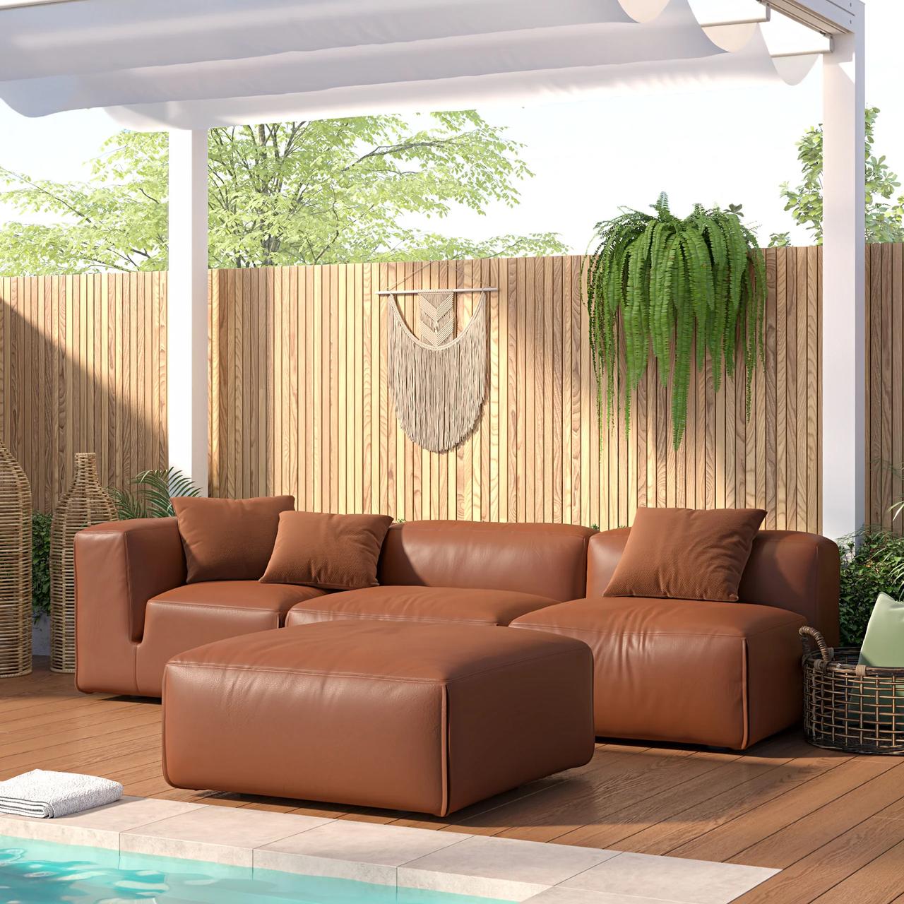 A plush brown 3d modular sofa and a matching ottoman are arranged on a sunlit patio beside a light blue swimming pool. Behind the seating area, a decorative wooden slat wall is adorned with a woven macrame piece and vibrant green hanging ferns under a white pergola.