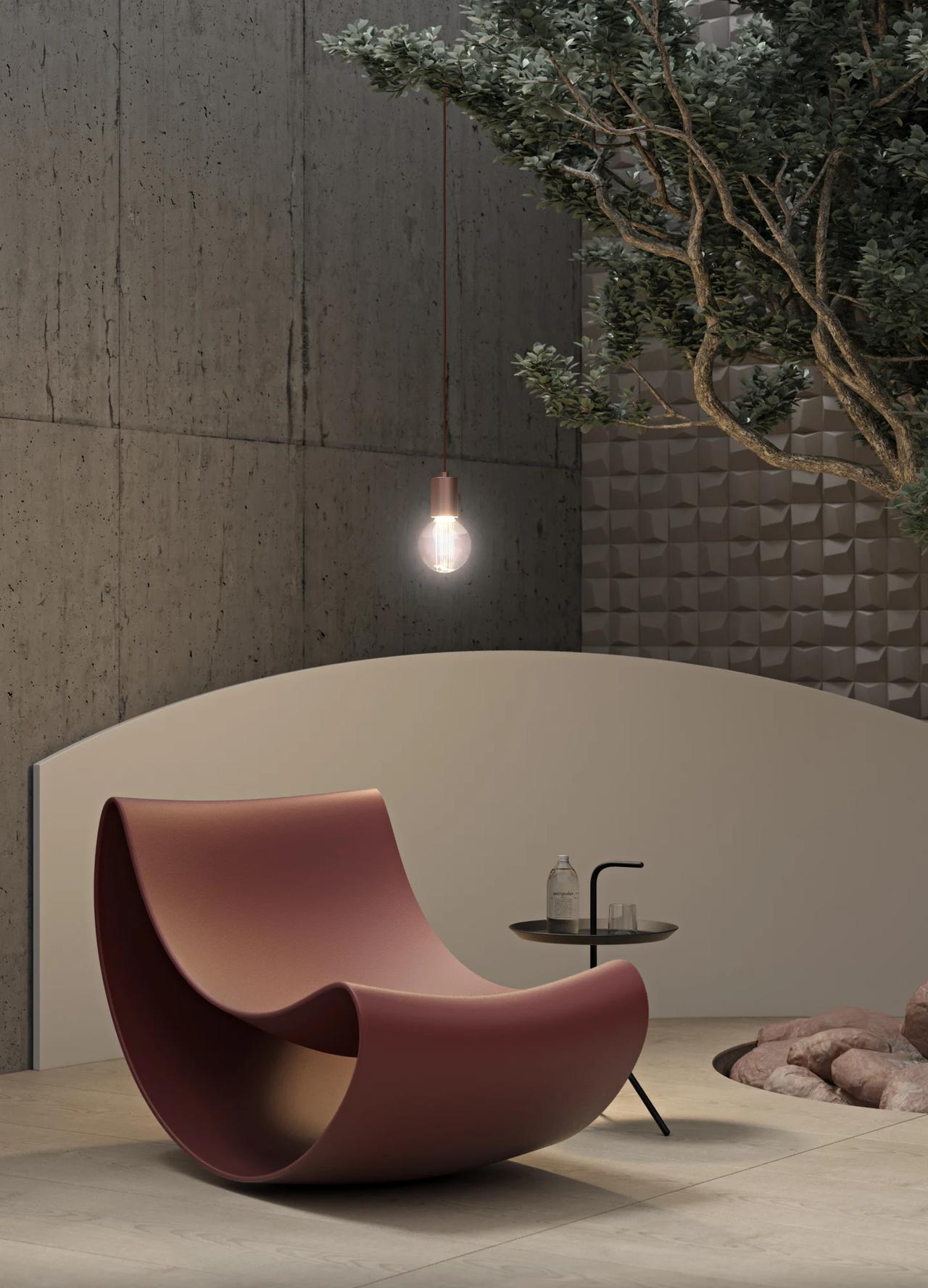 A artistic terracotta-colored curved rocking 3d chair positioned on a stone floor in a minimalist Japandi room. The background features a smooth curved wall, raw concrete textures, a indoor tree, and a simple warm hanging bulb.