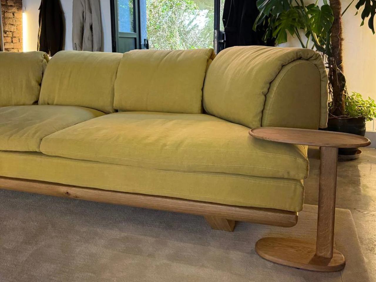 Modern mustard yellow upholstered sofa with a solid wooden base and a matching C-shaped wooden side table in a cozy showroom