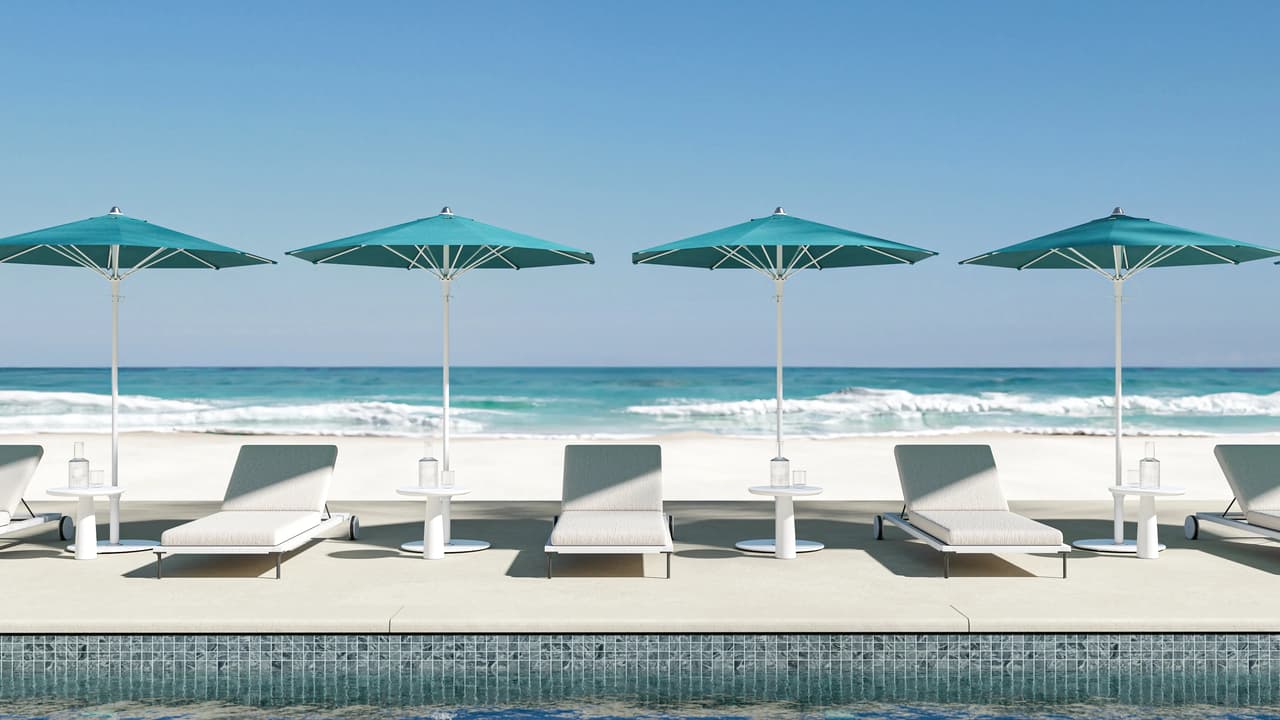 A perfectly aligned row of four turquoise octagonal 3d umbrellas shading white modern sun loungers and small side tables on a sunny patio. The foreground features a blue mosaic pool edge, while a pristine white beach and rolling ocean waves complete the tropical background.